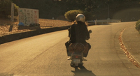 Signs with crude writing line the street as the main character drives to work on a scooter. One says, "Illegal dumpers are inhuman."