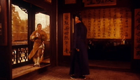 A man greets a visitor entering his home with banners with black calligraphy hanging on the wall.