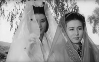 A black-and-white film still in a medium close-up shot. It shows two female figures with wearing muslin veils. The figure to the left has half of her face covered by her veil.