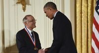 Figure 3. President Barack Obama shakes Bob Axelrod’s hand after presenting him with the Medal of Freedom. Obama faces slightly away from the camera. Both men are smiling.