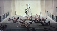 A still from a music video. Beyoncé and Jay-Z stand atop a grand staircase with a statue at their backs and dancers lying on the steps.
