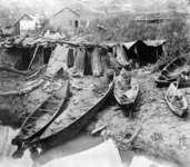 A black-and-white photograph of six dugout canoes of various sizes along a beach at Songhees Reserve.