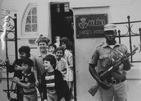 Fig. 28. An Frelimo armed soldier directly looks at an unidentified photographer as he pictures the soldier standing at a gate while students leave the school grounds with the assistance of a teacher.