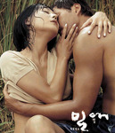 A film poster with white calligraphic text in the bottom right, over a background of a man and a woman sensually embracing in slight undress.