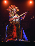 Performer Taylor Mac wearing glittery drag and playing a banjo while sitting on a stool during a performance of A 24-­Decade History of Popular Music in Brooklyn, New York.