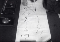 Black calligraphy is painted on white paper, in black and white cinematography.