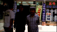 Men stand in front of stores with blue, red, white and black calligraphy printed on banners, signs, and the shop window glass.