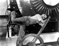 Fig. 38. Charlie Chaplin, as the Little Tramp, wearing overalls and T-shirt, is bent, struggling and overwhelmed, over a large lever next to a giant industrial machine.