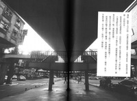 Black-­and-­white photograph of a skywalk footpath in Taipei underneath the Taipei Mass Rapid Transit System. Under the bridge, a pedestrian and cyclist cross the road while scooters and cars wait at the traffic lights. A textbox in Chinese on the right-­hand side of the photo describes the slow-­paced lifestyle of the urban Indigenous in contrast to modern city dwellers.