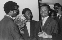 Igbokwughaonu Unamba-­Oparah stands with two other people wearing suits. All three are smiling and one looks at the camera.