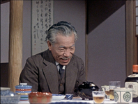 A scroll graces the tokonoma of a restaurant. It is barely visible behind one of the actors.