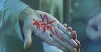 Close-up image of someone holding someone's hand that has red calligraphy painted on it.