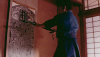 A man presents a sword towards a large calligraphy scroll hanging on the wall.