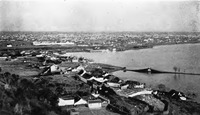 A black-and-white photo of a bird’s-eye view of a city, with a bridge spanning the right side of the photo.
