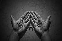 Black and white photo of a person’s hands laid out with their palms facing the viewer. The palms have shapes scratched into them. Between the hands there are two bullets, creating an arrow pointing upward.