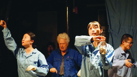 Figure 5.2: A color photograph of a medium close-­up of four actors during a theater performance, wearing blue factory-­workers’ overalls.