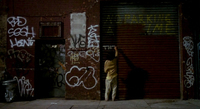 Protagonist writing on a wall covered with graffito.