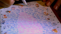 A letter has blue and pink calligraphy written on it, surrounded by stickers.