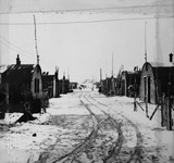 Muddy, snow-covered roads lined with houses in a refugee camp.