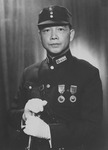 This black-­and-­white portrait shows Wang wearing a cap, military uniform, medals, and white globes, while holding a saber with both hands. He is turning slightly to the left while looking into the camera, solemn and unsmiling. He is wearing a leather shoulder holster diagonally across his chest, from right shoulder to left hip.