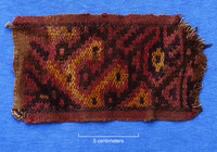 A photo of a cotton band with red, orange, brown, and black designs in wool.