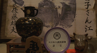 Names are brushed on a massive framed handprint on the wall. On a table before is sits a plate with the calligraphic character "Big. The style is evokes seal script, implying the family's lineage is ancient. There is also a decorative shogi piece with the backwards character for horse carved into the wood, called a "hidari uma," or "left horse." Uma read backwards—mau—means to dance, so this is a kind of good luck charm.