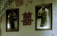Close-up image of a cutout of red calligraphy posted on a wall between two framed photos.