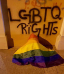 Graffiti in black paint on a wall in Beirut reads “LGBTQ Rights.” The “i” in “Rights” has three dots, similar to the Arabic letter. A rainbow flag lies crumpled beneath it. In the background, faded red graffiti written in Arabic are still visible.