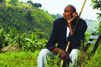 A portrait of a Rwandan man sitting in a chair with a long stick resting his lap.