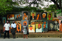 Photograph of painted portraits stacked along a sidewalk