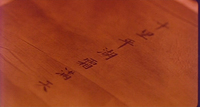 Close-up image of a piece of wood with delicate brown calligraphy written in a single line.
