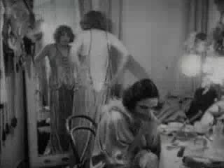 A black and white silent film clip, including quick cuts of a revue performance. The quick cuts include the dancers preparing, the audience waiting in the theater, followed by the orchestra starting to play. There are several cuts between dance numbers, acrobatics, bicycle tricks, juggling, and a kickline. The clip ends with the performance ending and the audience leaving the theater, out into the night street.