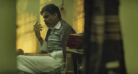 Medium shot of a mirror showing Siras (Manoj Bajpayee) in profile, with a tape deck and nightcap by his side. He appears lost in music, with his eyes closed and hand extended in front of his face, in a gesture of appreciation.