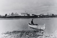 Solitary paddler sits in a birch-bark canoe at Moose Factory, Ontario.