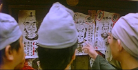 Image of four people pointing at posters on a wall. The posters feature drawings of people along with handwritten black calligraphy, some circled in red.