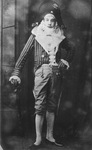 Georges wearing a bicorne hat, striped jacket with broad white collar, knee pants, and white stockings, leaning against a cane.