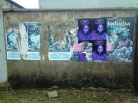 Photograph of concrete wall covered with torn paper posters with film titles and images