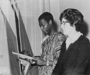 Dr. J.K. Nsarkoh looks down at the paper in his hand while standing beside Miss Middell.