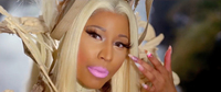 Figure 21. Nikki Minaj appears in extreme close-up with blond hair, prominent false eyelashes, and pink lipstick. She wears an elaborate head dress and gestures toward her face with the ornate fingernails of her left hand.