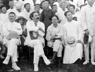 This black-­and-­white photo shows four seated figures, all clad in white, surrounded by an unknown number of people, mostly civilians similarly dressed in white. On the left side of the front row there is Vasily Blyukher, with close-­cropped hair and a mustache. He is sitting with crossed arms and legs while looking to the left. Borodin and Wang both look to the right. Borodin, his hair brushed back and wearing a grin beneath the mustache, sits crossed legged, his arms resting on his gray hat. Zhang Tailei, young, bespectacled, and short, is seated between them but slightly withdrawn, looking directly at the camera. Wang is in a long white robe with a white fedora resting on his knees. Blyukher and Zhang look tense; Borodin, relaxed; Wang, calm.
