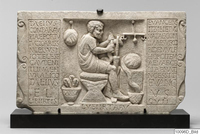 Within a scrolled frame, two panels of inscribed text surround a square relief depicting a bearded man seated, facing right. He is surrounded by implements of work, including a scale and baskets, and works pulling cloth or fiber toward himself.