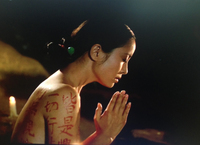 A woman with a sutra painted on her body prays.