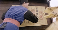 A man leans in front of a wide poster with calligraphy.