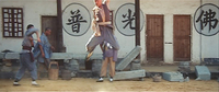 A man leaps into the air in the street, with calligraphy painted on the walls of the buildings behind.