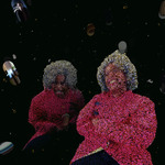 Detail still image of installation: Left center is the image of a woman with dark-brown skin. The figure comprises black-eyed peas. She has short white hair and wears a red outfit. She is laughing. Right center is a similar image of the same woman. She is screaming. Both women appear to be floating in outer space on a black background. Orbs with faces are circling around them.
