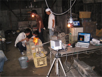 手前の三脚に載っているカメラが非接触温度測定装置の本体，その右にある机の上のパソコンには温度測定画面が表示されている。