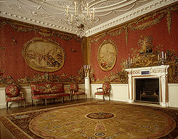 Designed for the Earl of Coventry by Robert Adam, the room features walls lined with tapestries and similar-looking upholstery. A novel aspect is the continuous tapestry on all four walls, in effect a pictorial wall covering rather than a framed, painting-like tapestry. The scenes in the cartouches were designed by Boucher; the tapestries woven in Jacques Nielson's atelier at Gobelins. "Aux alentours" (with borders) refers to the production technique, whereby a detailed scene was fit into a plainer, more quickly executed surrounding.